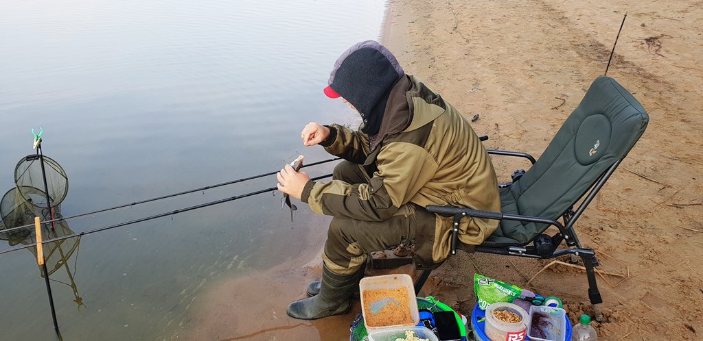 Рыболов с фидером на водохранилище наживляет наживку на крючок Рыболов с фидером на водохранилище наживляет наживку на крючок
